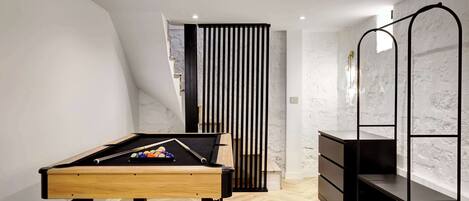 Una habitación moderna con una mesa de billar, un estante metálico negro y una pared blanca con textura.