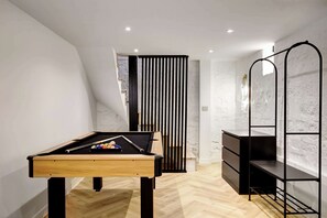 A modern room with a pool table, a black metal shelf unit, and a white textured wall.