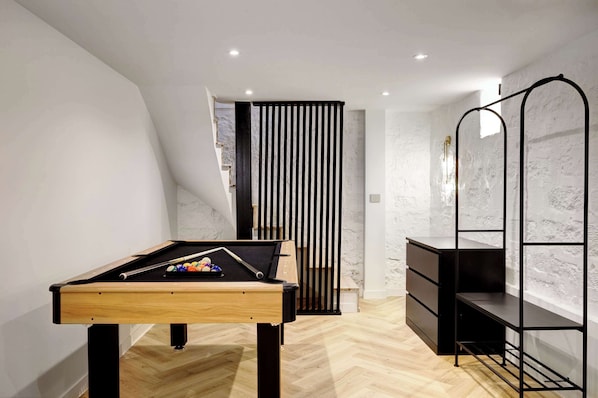 Ein modernes Zimmer mit Billardtisch, einem schwarzen Metallregal und einer weißen, strukturierten Wand.