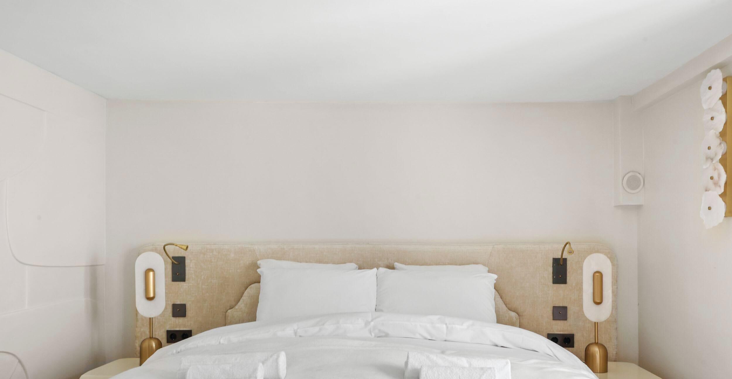 A bedroom with a bed, two bedside tables, and a wall-mounted light fixture.