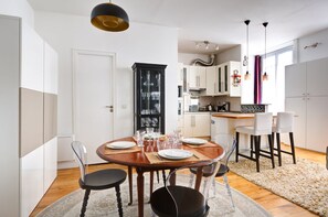 A modern kitchen with white cabinets, a black cabinet with glass doors, and a dining area with a wooden table set for four.