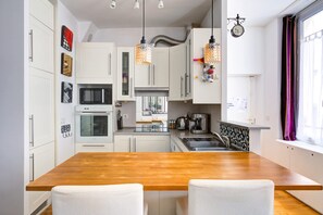 A modern kitchen with white cabinets, a wooden table, and pendant lights.