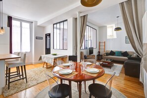 A modern living room with a dining area, large windows, and a sofa.