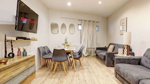 Un soggiorno moderno con TV a schermo piatto, un'area pranzo con sedie e tavolo, e un divano grigio.