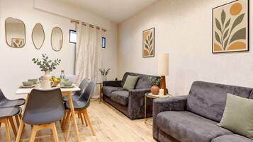 Una sala de estar moderna con un sofá gris, una mesa de comedor con sillas y una mesita auxiliar con una lámpara.