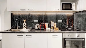 Una cucina moderna con mobili bianchi, una parete di fondo in marmo nero ed elettrodomestici in acciaio inossidabile, tra cui un forno a microonde, un tostapane e un forno.