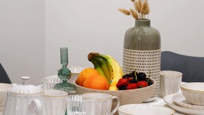 Un tavolo da pranzo con una ciotola di frutta, un vaso con piante secche e diverse ciotole e tazze di ceramica bianca.