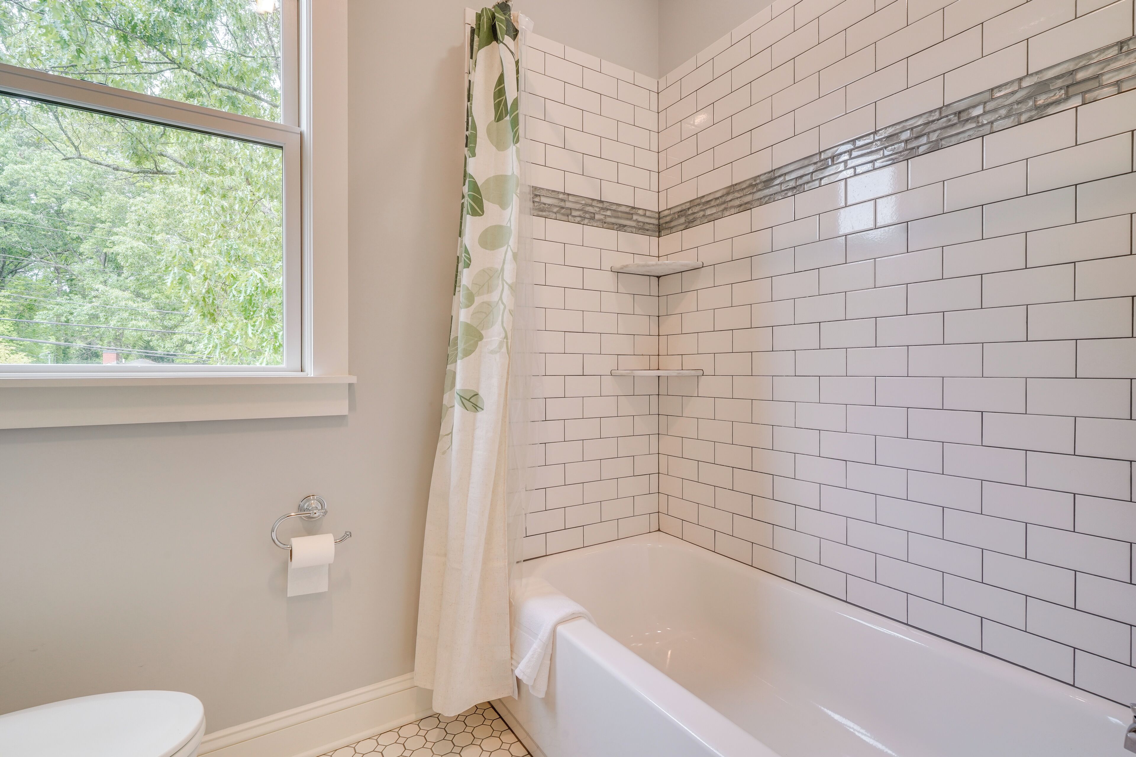 A bathroom with a white bathtub, a window with a view of trees, and a toilet with a paper towel holder.