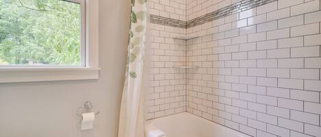 A bathroom with a white bathtub, a window with a view of trees, and a toilet with a paper towel holder.