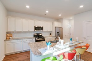 A modern kitchen with white cabinets, stainless steel appliances, a granite countertop, and colorful bar stools. - Colorful Myrtle Beach House: 2 Mi to Beaches! (Myrtle Beach)