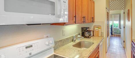 A kitchen with a microwave, stove, sink, and wooden cabinets.