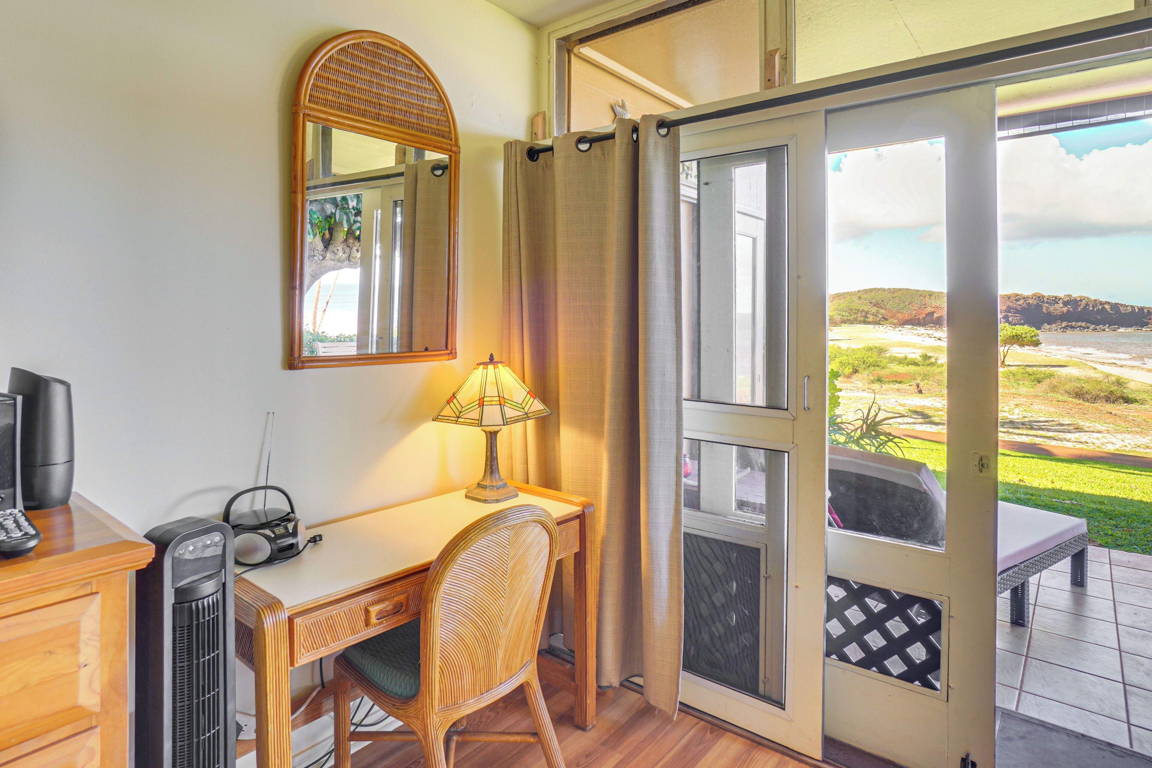 Habitación con escritorio, silla, radio y vista de un paisaje a través de una puerta corredera.