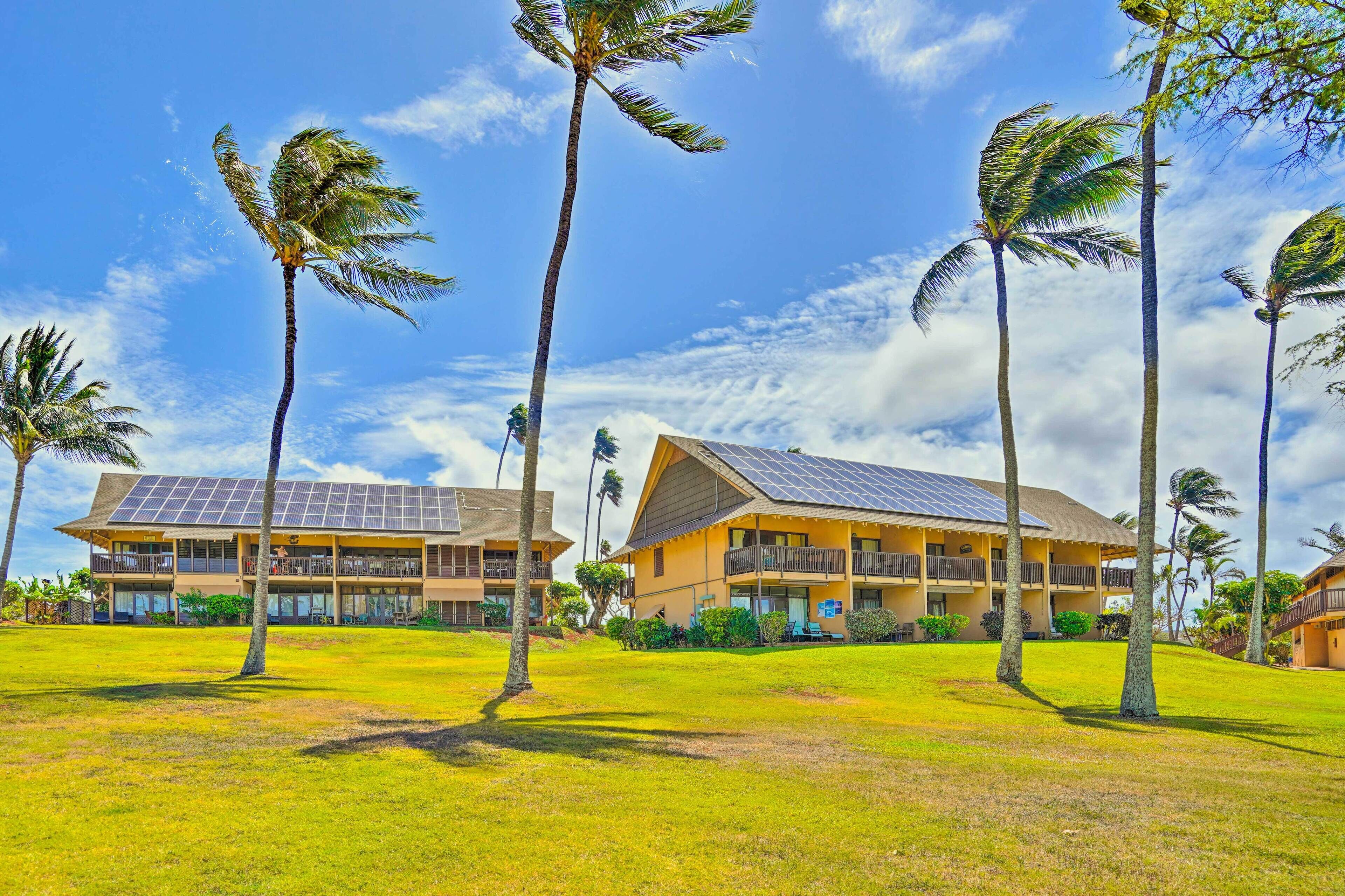 A hotel with a two-story building, solar panels on the roof, and a grassy lawn with palm trees.