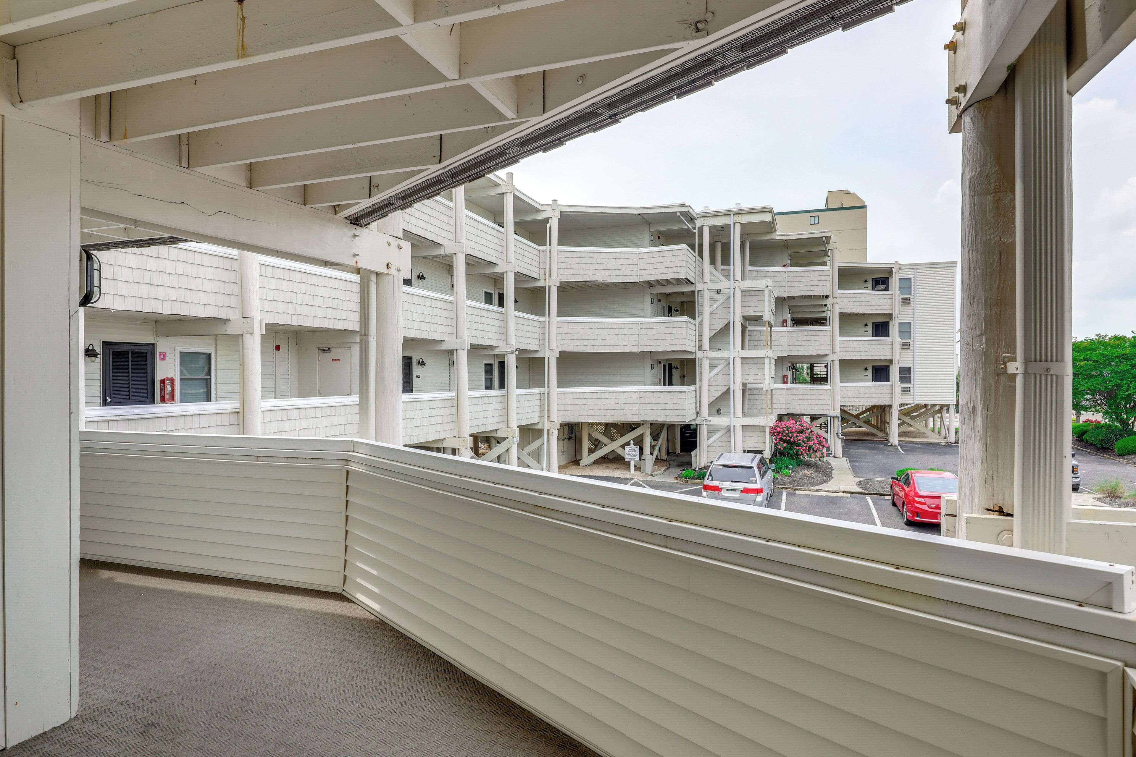 A multi-story building with a white exterior, balconies, and a parking area with cars.