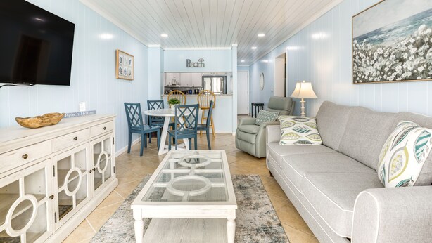 A living room with a sofa, coffee table, TV, and a dining area with chairs and a table. - 1 Mi to Barefoot Landing: Condo w/ Pool Access! (North Myrtle Beach)