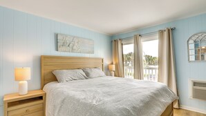 A bedroom with a wooden headboard, a bed with a grey blanket, two bedside lamps, a nightstand with drawers, and a window with curtains. - 1 Mi to Barefoot Landing: Condo w/ Pool Access! (North Myrtle Beach)