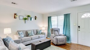 Un salon avec un canapé gris, un fauteuil inclinable gris, un pouf noir et une porte blanche.