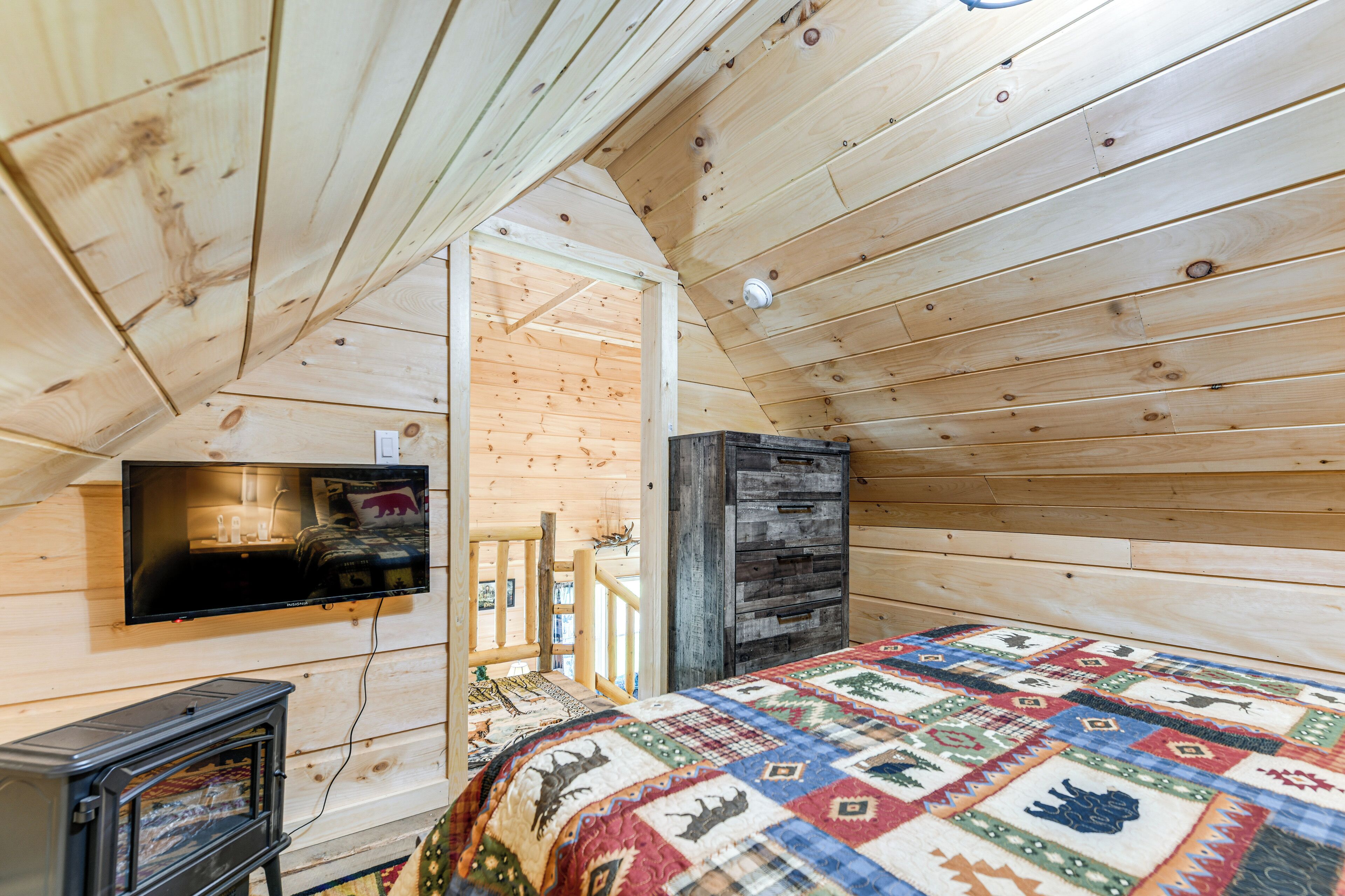 Une chambre confortable de style cabane, avec un plafond en bois, un téléviseur fixé au mur, une courtepointe et une petite cheminée.
