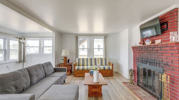Relax in this stylish living room with a large sofa, armchair, and coffee table, featuring a cozy fireplace and large windows.