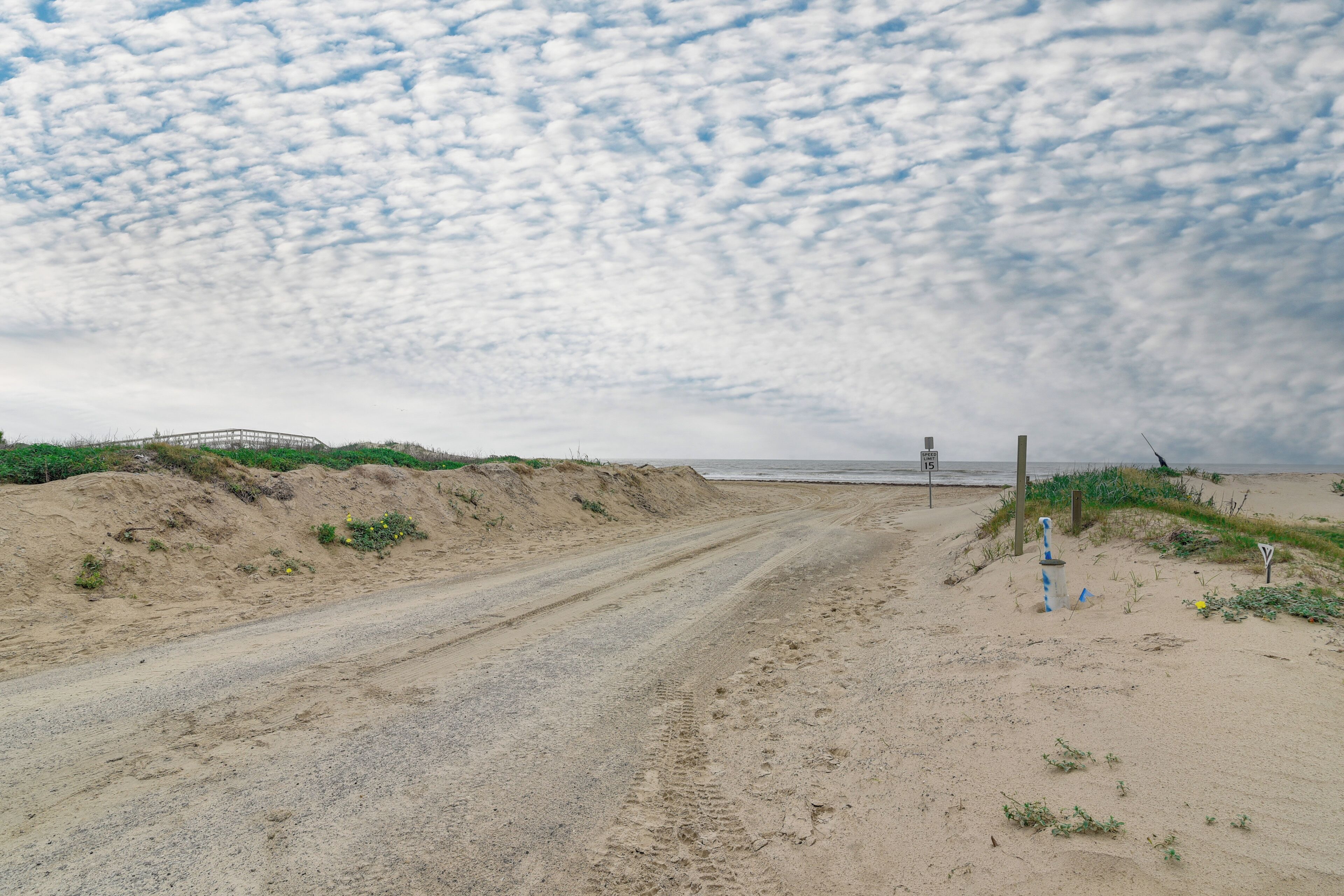 Ein sandiger Strand mit einem Feldweg, der zu einer Struktur in der Ferne führt.