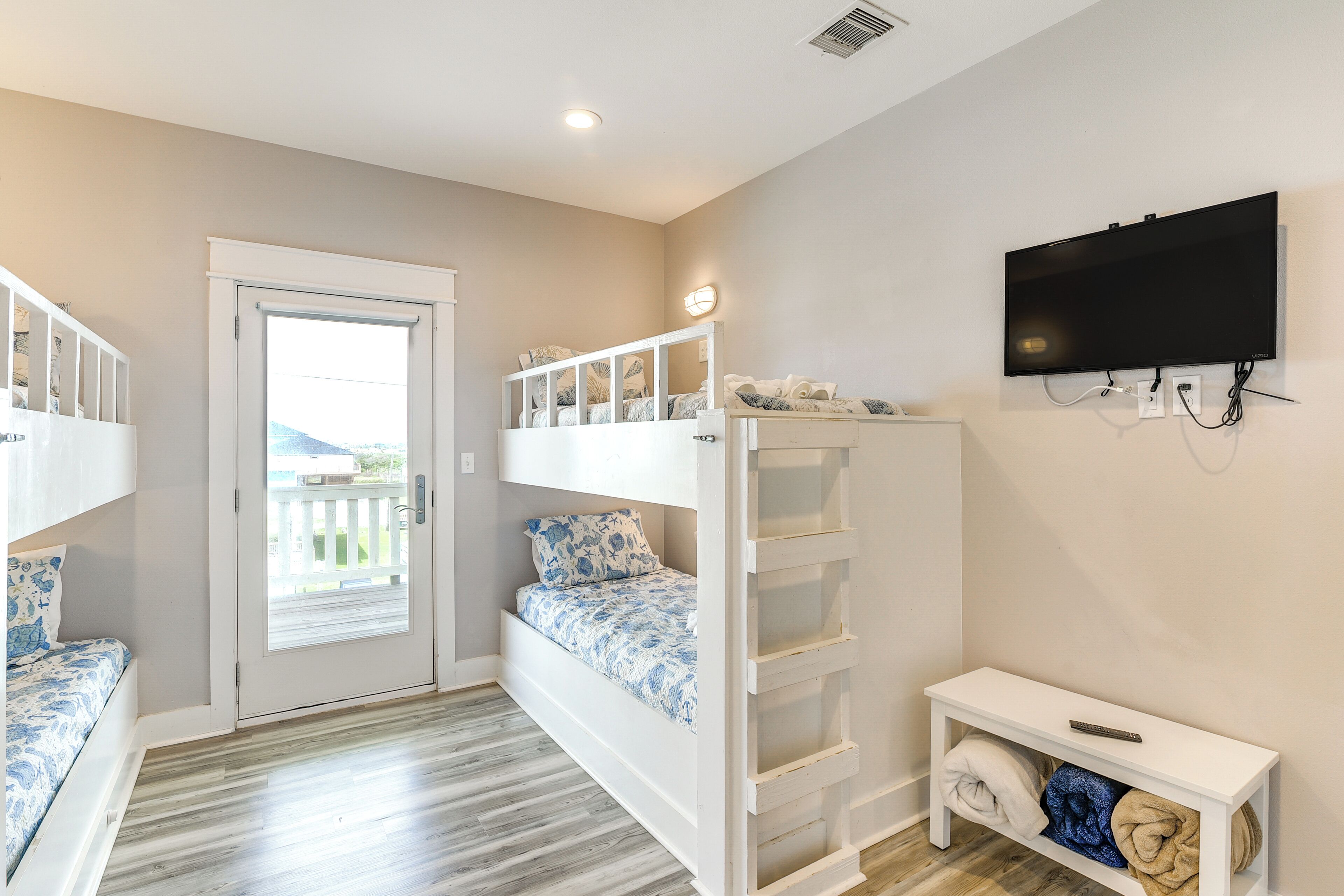 A room with bunk beds, a television, and a bench with blankets.
