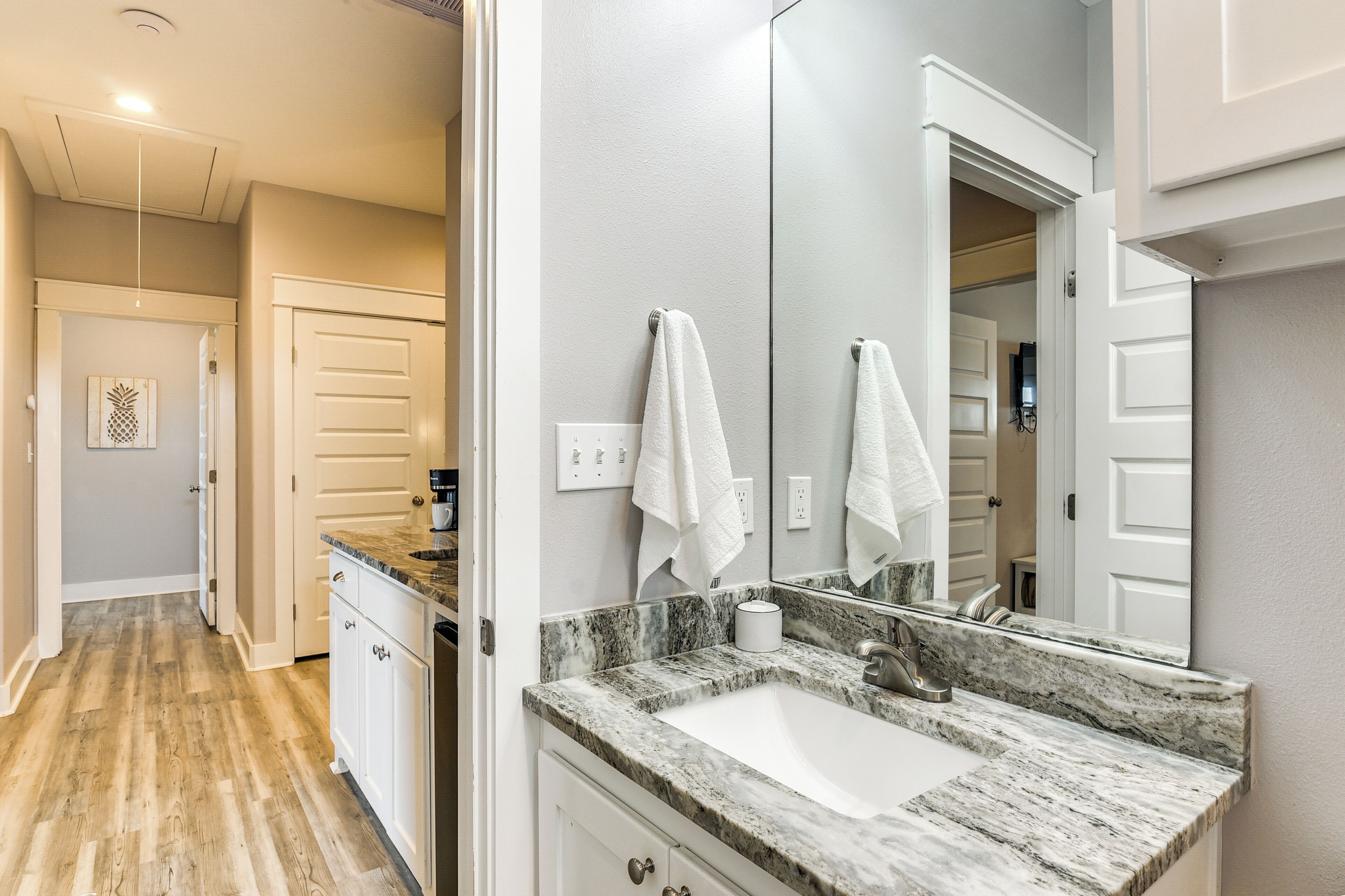 A modern bathroom with a marble countertop sink, a large mirror, and white towels hanging on the wall.