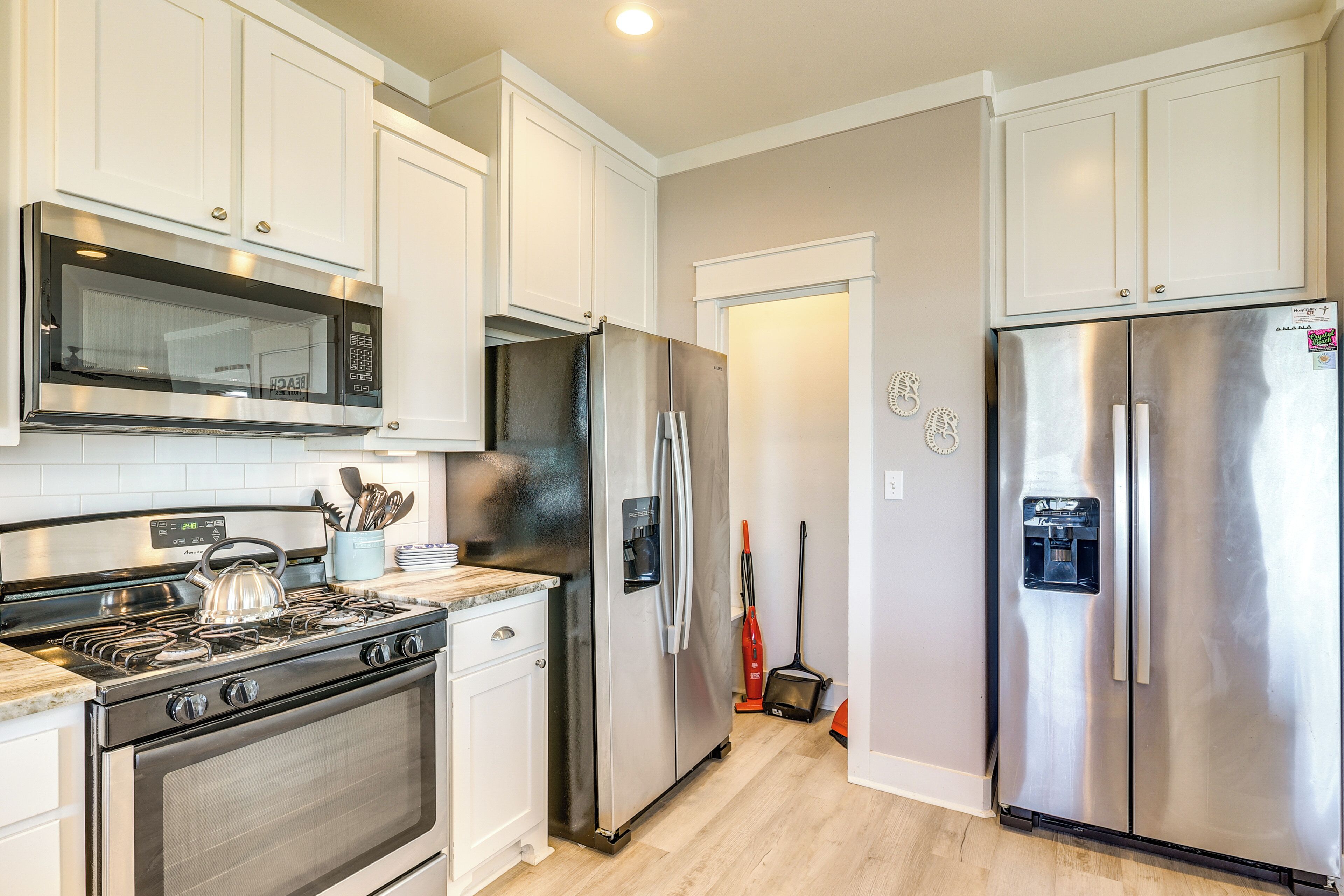 A modern kitchen with stainless steel appliances, white cabinetry, and a tiled backsplash.