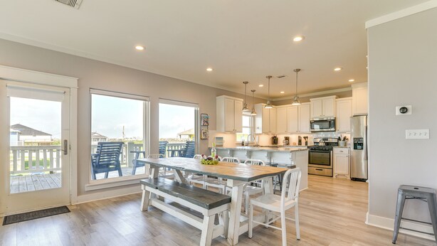 A modern kitchen with white cabinets, stainless steel appliances, and a wooden dining table with benches. - 1 Block to Shore: Crystal Beach Gem, Deck & Views (Port Bolivar)
