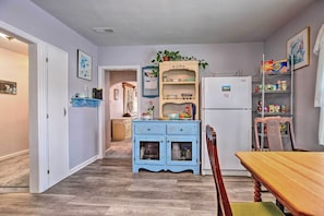 A kitchen with a blue cabinet, wooden table, and chairs. There is a refrigerator and a shelf with various items. - Cozy Cedarburg House - Walk to Historic Downtown! (Cedarburg)