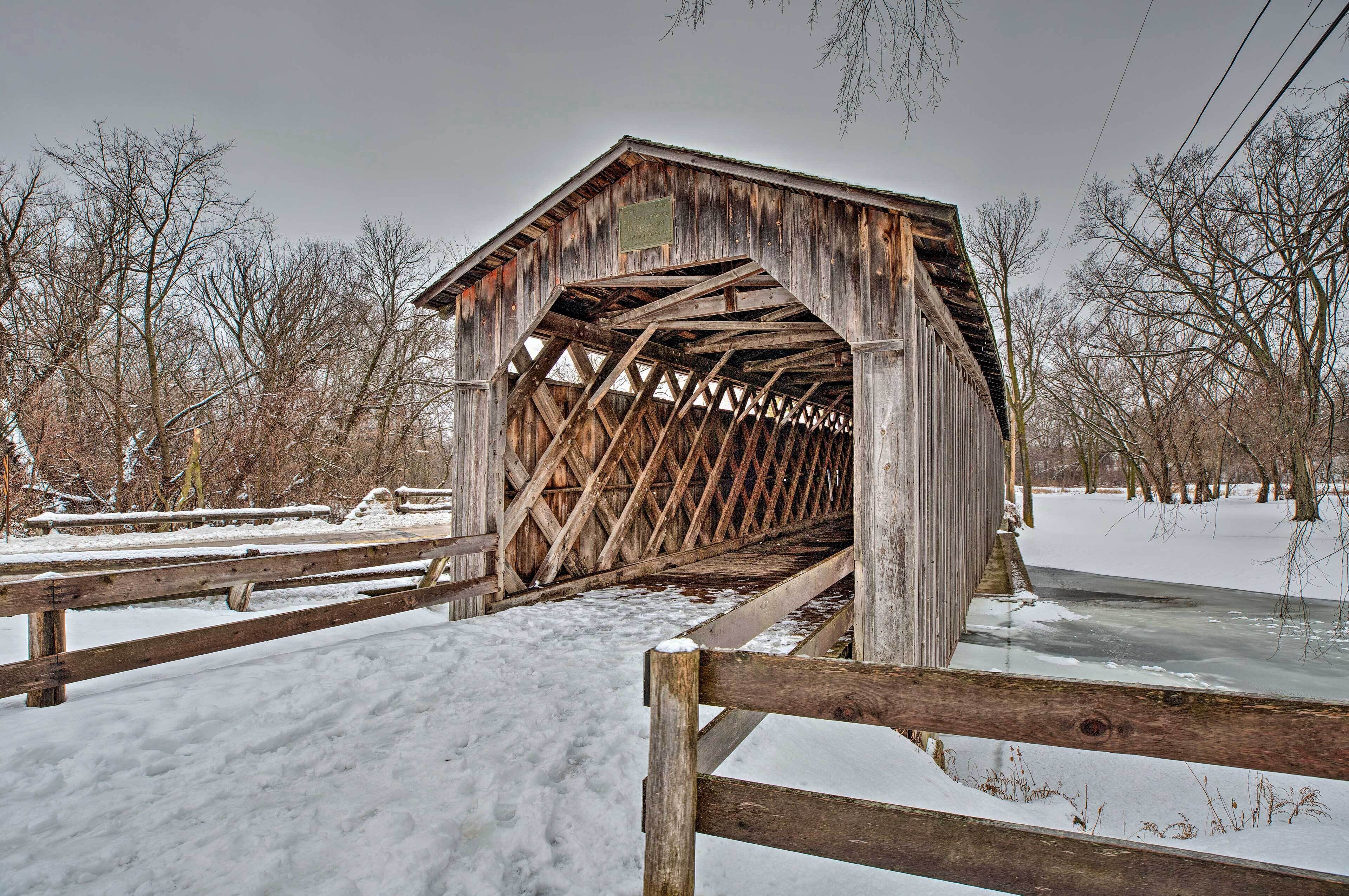 A wooden covered bridge with a metal roof, surrounded by snow-covered ground and leafless trees.