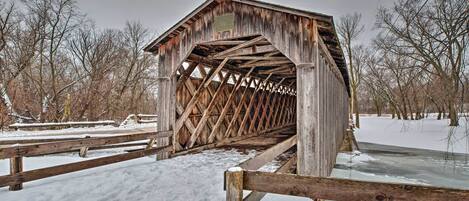 A wooden covered bridge with a metal roof, surrounded by snow-covered ground and leafless trees.