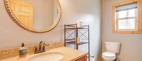 A bathroom with a granite countertop sink, a wooden vanity, a freestanding toilet, a towel rack, and a window with a wooden frame.