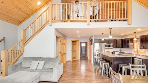 A spacious living area with a wooden staircase, a grey sofa, and a kitchen with a bar area. - Pet Friendly Lake House: Waterfront w/ Boat Dock (Eagle River)