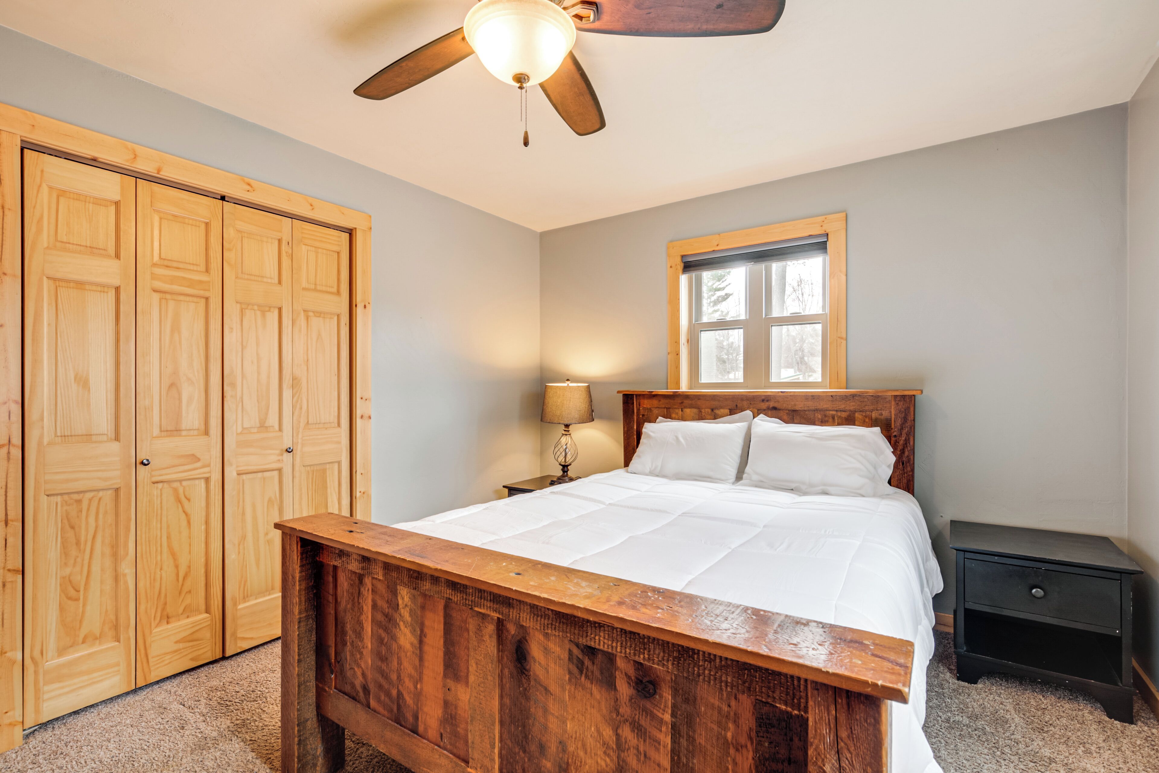 A bedroom with a wooden bed, a ceiling fan, a nightstand, and a window.