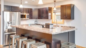 A modern kitchen with stainless steel appliances, granite countertops, and bar stools. - Pet Friendly Lake House: Waterfront w/ Boat Dock (Eagle River)