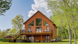 A two-story wooden cabin with a balcony, a covered porch, and a swing set in the yard. - Pet Friendly Lake House: Waterfront w/ Boat Dock (Eagle River)