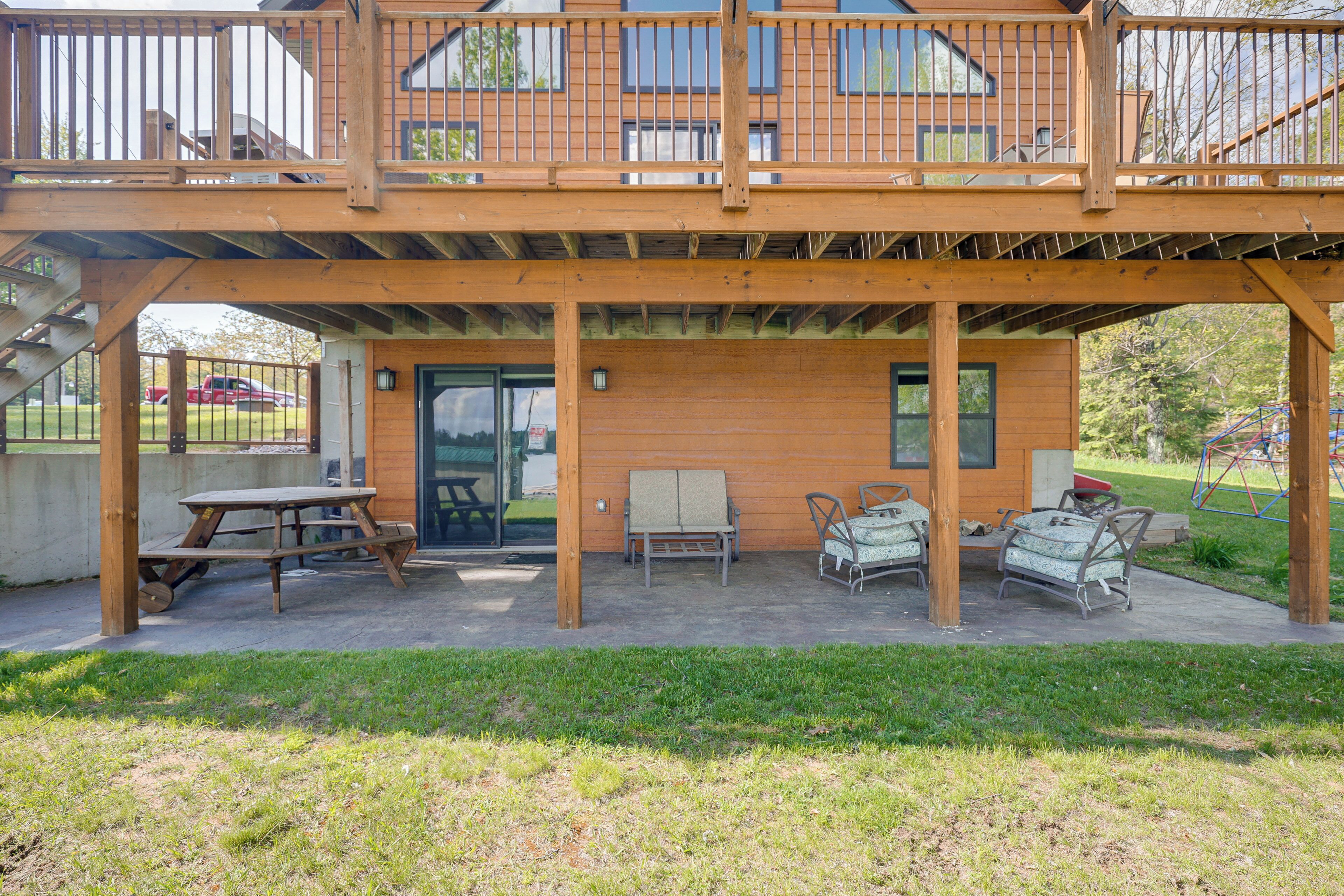 Un terrazzo in legno con tavolo e sedie da picnic, un'area patio coperta e vista su un edificio residenziale.
