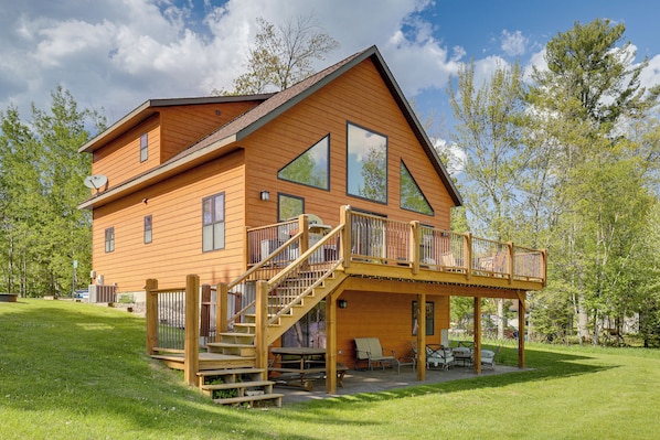 A two-story wooden house with a balcony, a staircase, and a patio area with outdoor furniture. - Pet Friendly Lake House: Waterfront w/ Boat Dock (Eagle River)
