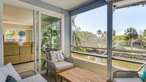 Ein Balkon mit Korbmöbeln, einem Holztisch und Blick auf ein Gewässer und viel Grün.