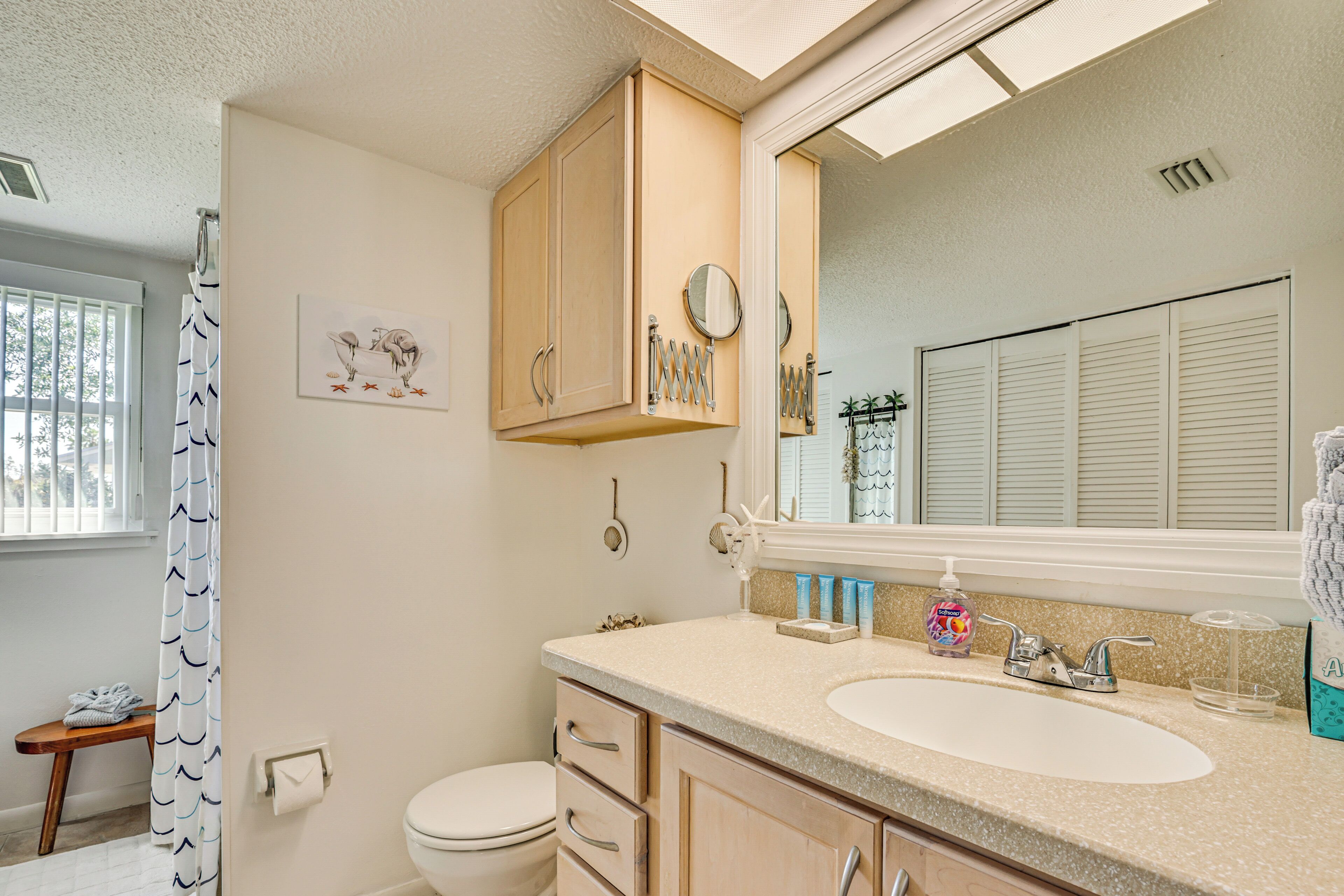 A bathroom with a toilet, sink, mirror, and wooden cabinets.