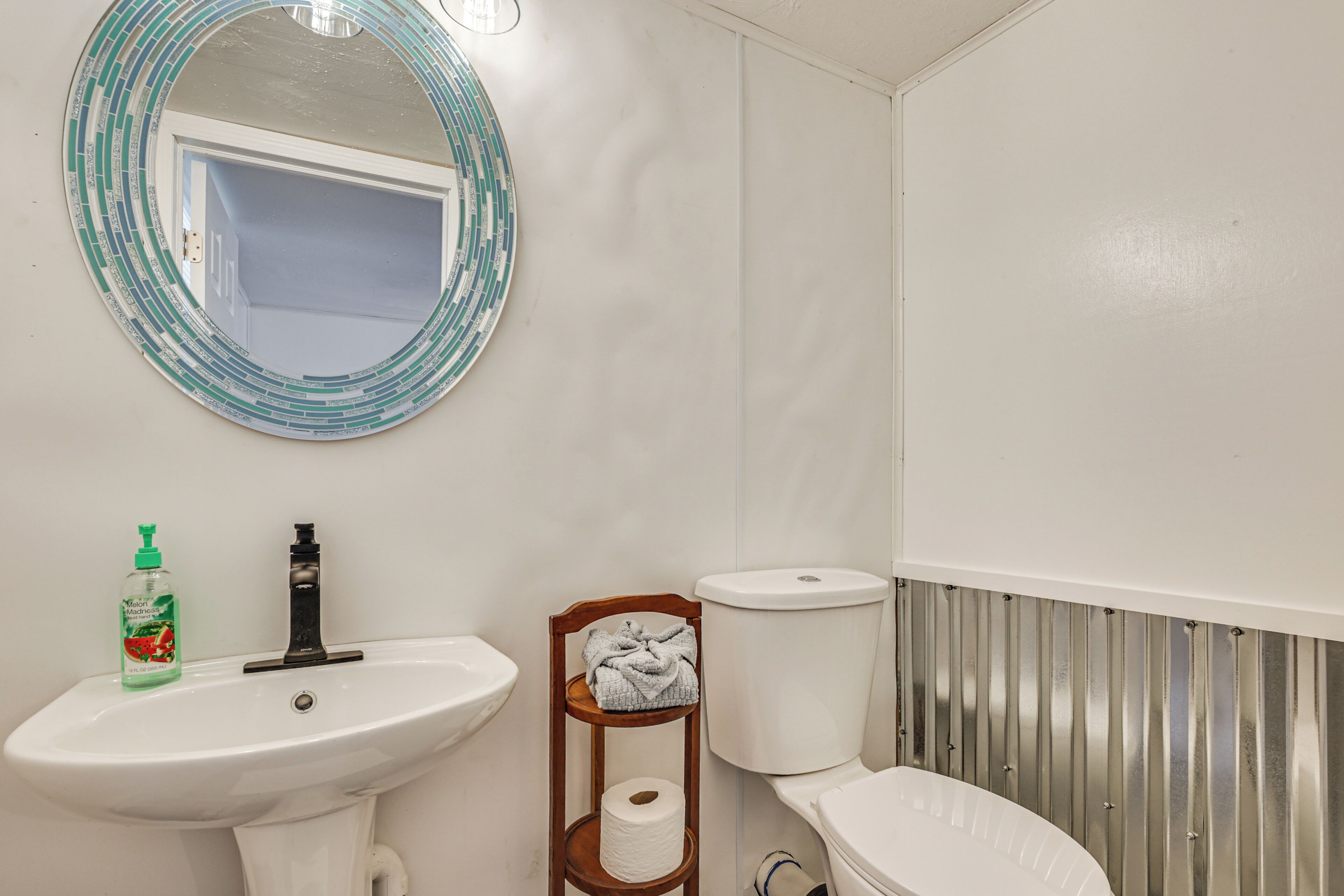 A bathroom with a white sink, a mirror with a blue frame, a toilet, and a wooden shelf with a towel.