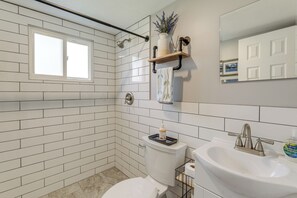 A bathroom with white subway tiles, a toilet, a sink with a faucet, a window, and a shelf with a plant and a towel.