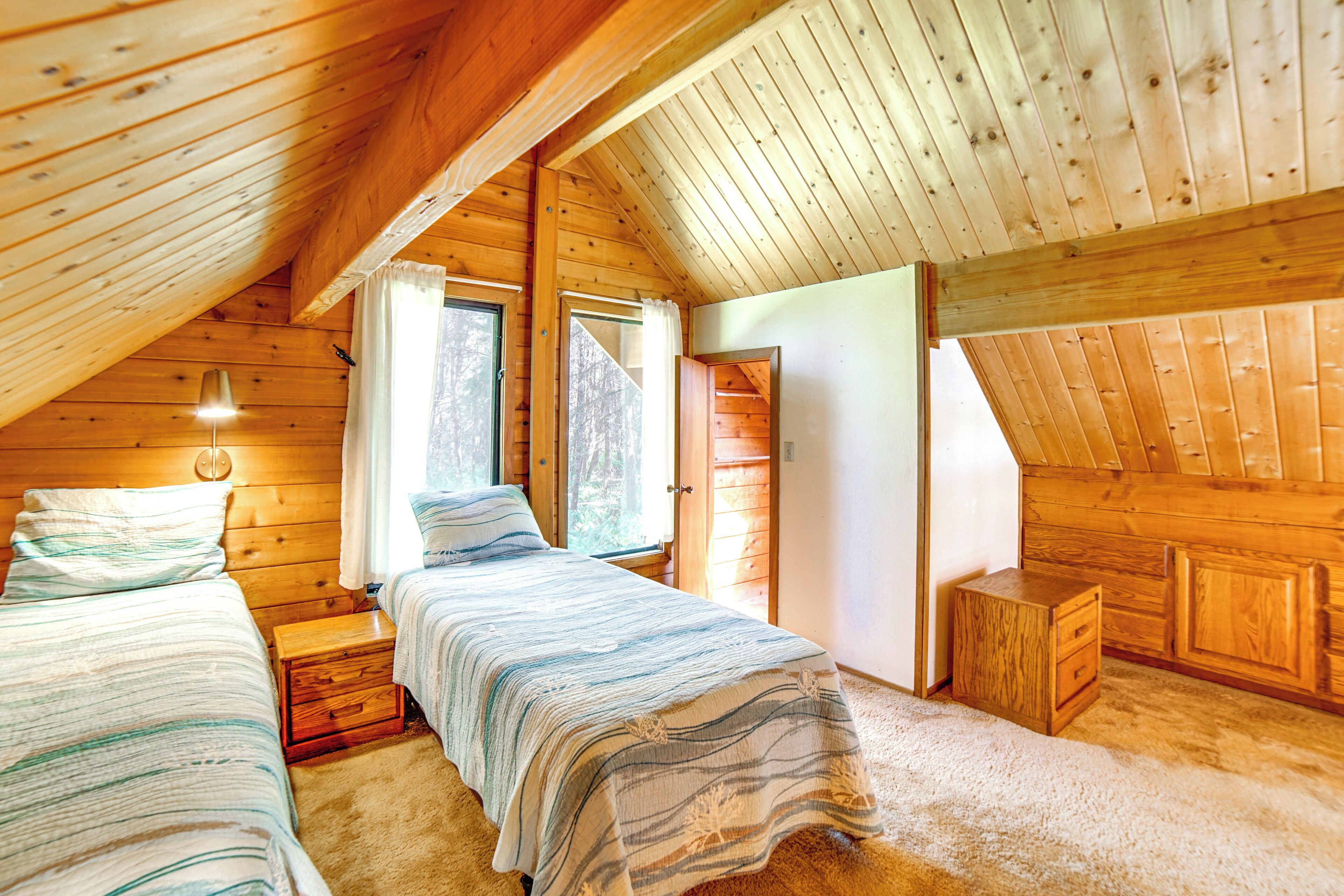 A cozy attic bedroom with two beds, a small wooden nightstand, and a window with curtains.