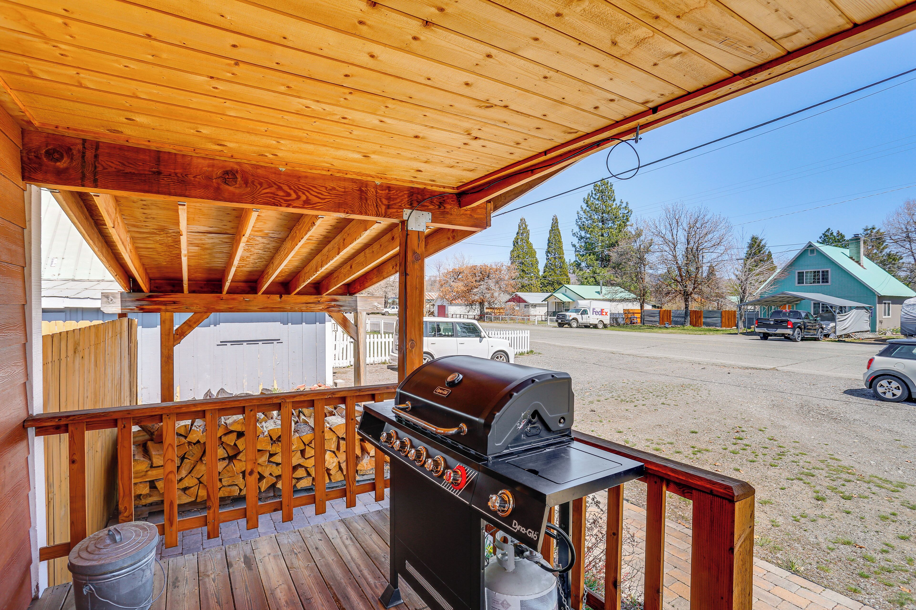 Una terraza cubierta de madera con una parrilla, una cerca de madera y vistas a una calle con coches aparcados y casas.