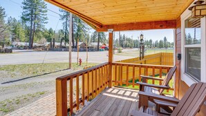 Eine Holzterrasse mit überdachter Veranda, Sitzgelegenheiten im Freien und Blick auf eine Straße und einen Wald.