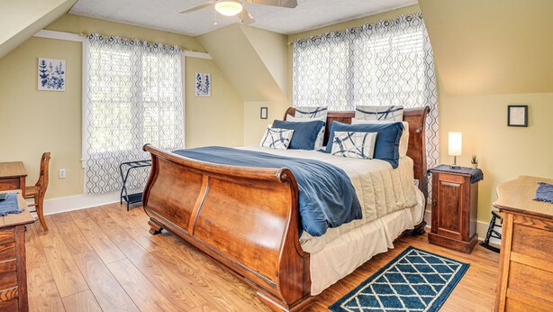 A bedroom with a wooden bed, a ceiling fan, and a window with patterned curtains. - 1 Block to Crescent Lake: Charming Home w/ Porch! (Crescent City)
