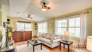 A living room with a sofa, coffee table, and side tables. There are windows with curtains, a ceiling fan, and a wooden floor. - 1 Block to Crescent Lake: Charming Home w/ Porch! (Crescent City)