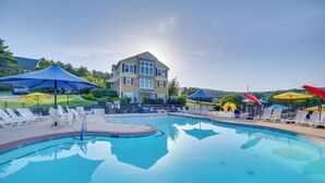 Ein Swimmingpool mit Liegestühlen und Sonnenschirmen, ein großes Gebäude im Hintergrund und ein klarer Himmel.