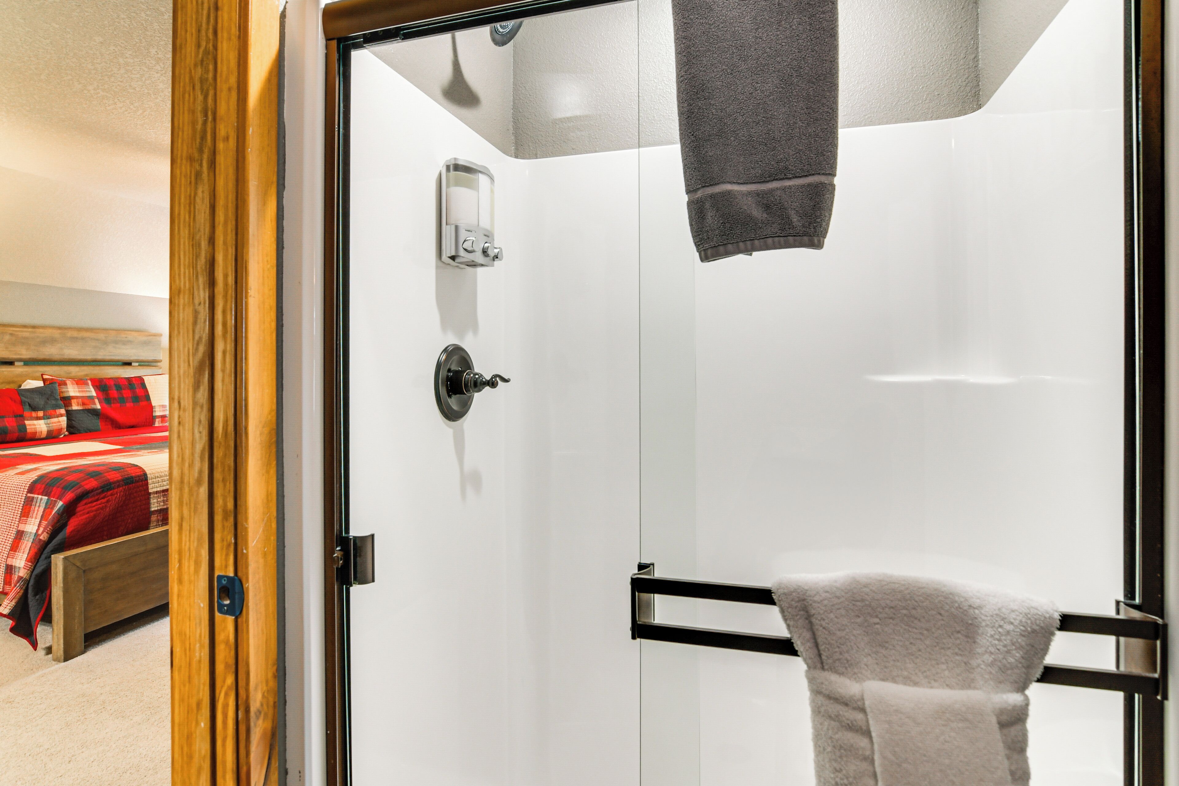 A bathroom with a glass door, a towel rack, and a soap dispenser.