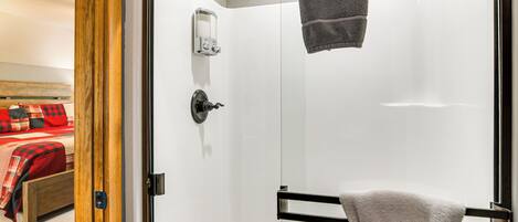 A bathroom with a glass door, a towel rack, and a soap dispenser.